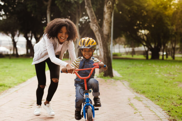 Mulher adulta ensinando seu filho pequeno a andar de bicicleta.