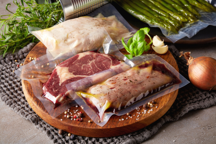 Carnes embaladas à vácuo, dispostas em uma tábua redondo da madeira. Ornamentado com ervas frescas, sal e pimenta.