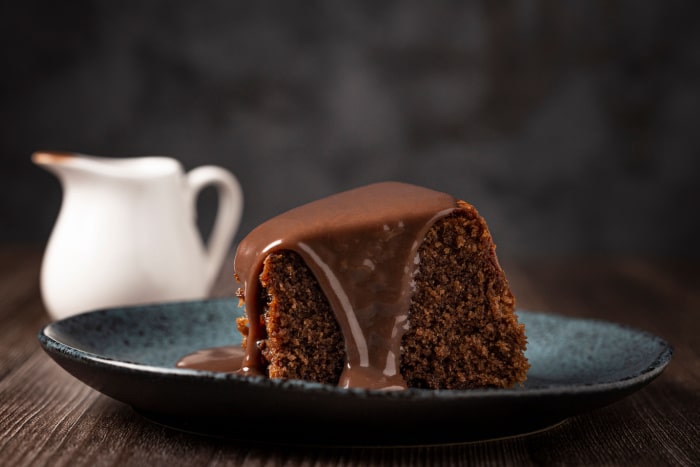 Pedaço de bolo de chocolate vegano com calda de chocolate escorrendo pelos lados.