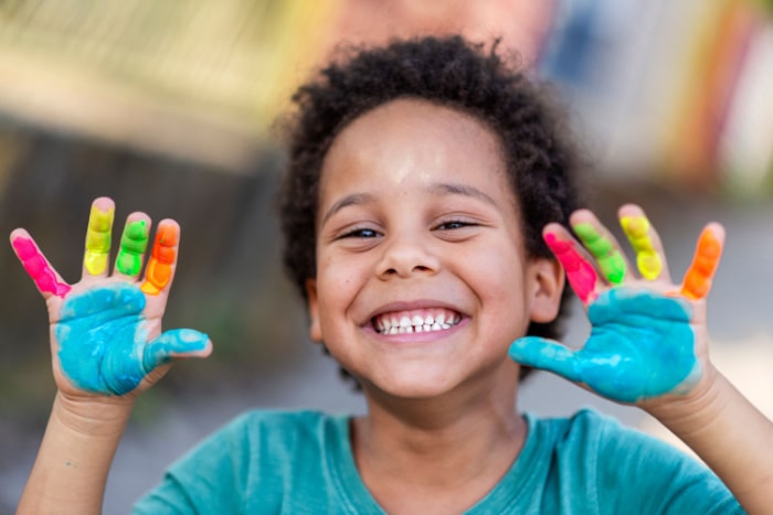 Criança com as mãos coloridas de tinta enquanto brinca de pintar.